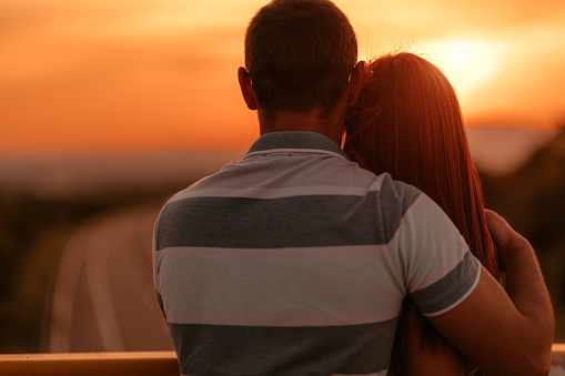 Young heterosexual loving couple enjoying at view at sunset from bridge.