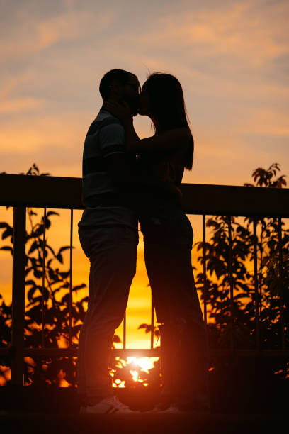 Couple silhouette kissing at sunset Young heterosexual couple silhouette kissing at sunset. kissing on the mouth stock pictures, royalty-free photos & images