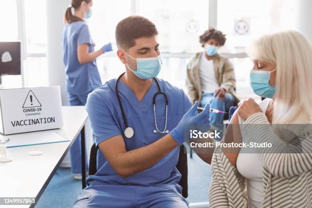 Mature Lady Receiving Vaccine Injection In Arm In Health Center Stock Photo - Download Image Now