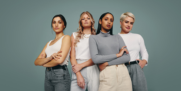 Group of fashionable women standing together in a studio. Diverse women looking at the camera while standing against a studio background. Four female friends looking confident in a studio.
