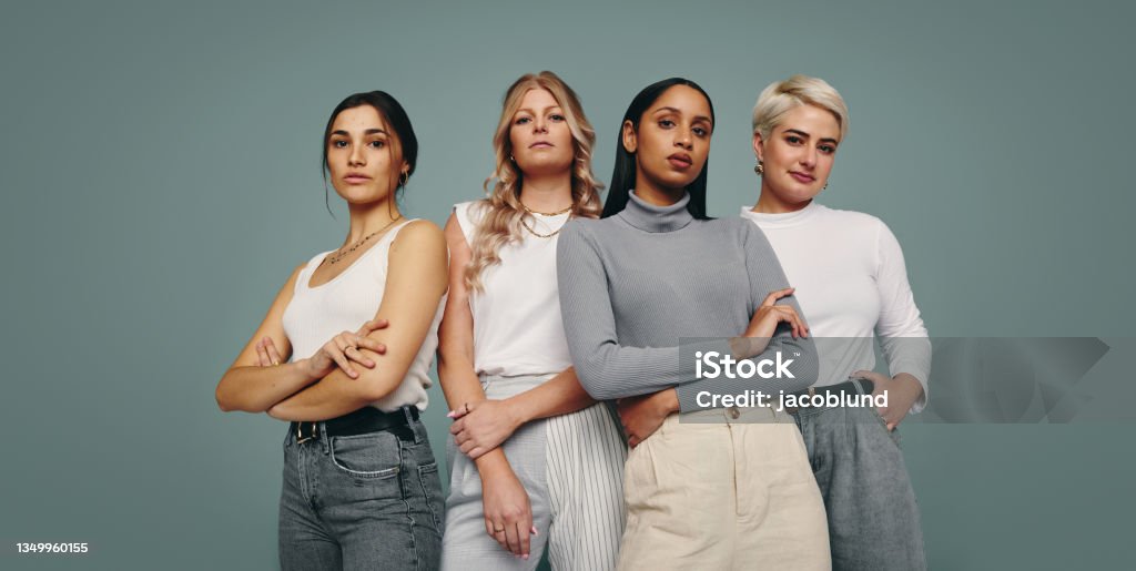 Group of fashionable women standing in a studio Group of fashionable women standing together in a studio. Diverse women looking at the camera while standing against a studio background. Four female friends looking confident in a studio. Women Stock Photo