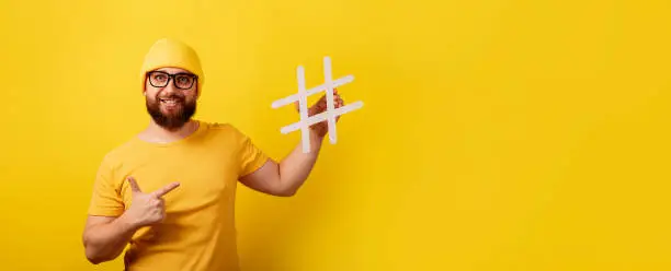 Photo of smiling bearded man pointing on hashtag