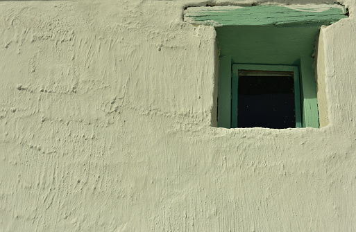 A small old-fashioned window with green wooden frame in a whitewashed wall