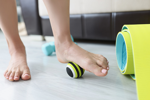Female legs roll small sports ball on floor at home closeup. Flat feet treatment concept