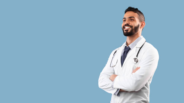 young middle-eastern doctor man crossing hands looking aside, blue background - aside imagens e fotografias de stock