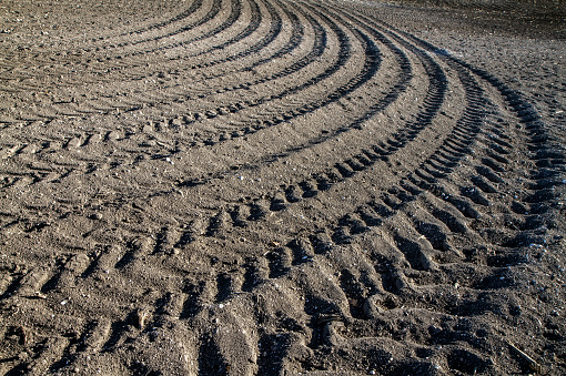 Horizontal photograph of brown dirt or mud patch or sand gravel pitch with tyre markings design, tire treads or grooves or patterns with shallow large marks making small pits