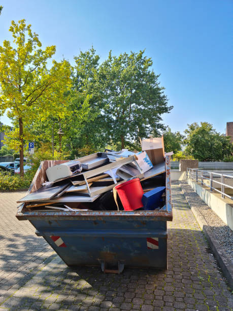A full rusty metal skip container with rubbish stands on the street in the parking lot near the house. The container contains old broken furniture, damaged household appliances, plastic, buckets and other rubbish. stock photo