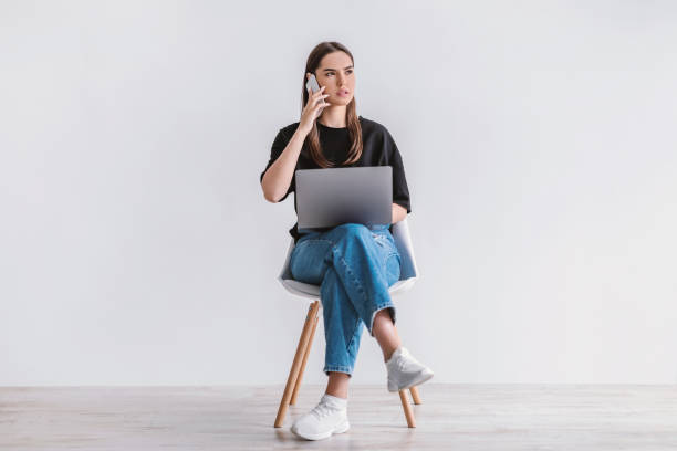 istock Troubled young woman with laptop sitting on chair, making phone call, having problem with online work or studies 1349968217