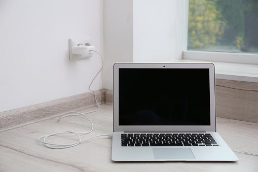 Modern laptop with charger on floor near white wall