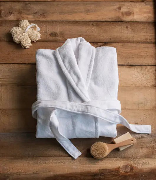 Photo of bathrobe bath soap and loofah brush behind wooden table