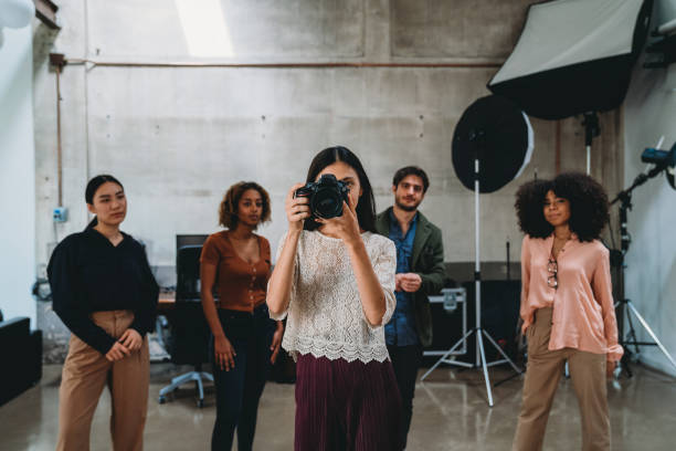 A woman photographer in her studio with a camera. People in the background.