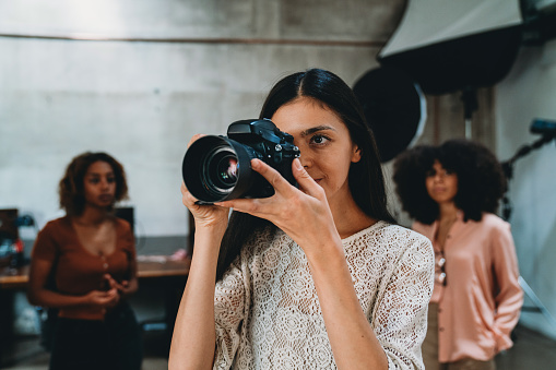 A woman photographer in her studio with a camera. People in the background.