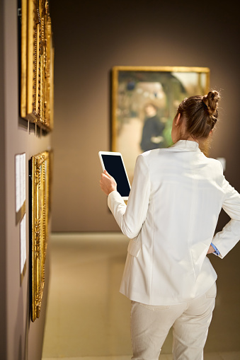 A young beautiful woman looking at painting in an art gallery.