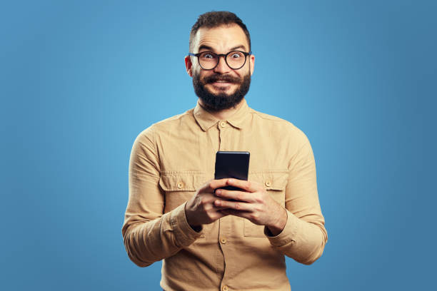 istock Man looking at camera while holding mobile phone, isolated over blue background 1349977327