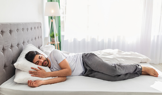 Full body length of calm arab man sleeping well on the side, resting, enjoying fresh cotton bedding, soft pillow and comfy mattress, banner, free space