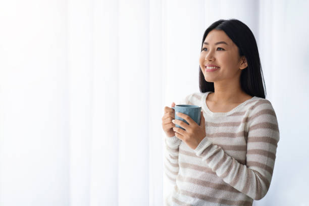 istock Relaxed Korean Female Drinking Coffee While Standing Near Window At Home 1349982765