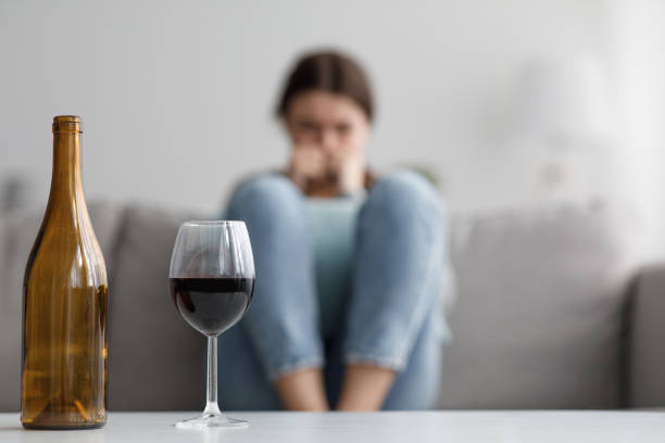 la triste femmina millenaria caucasica si siede sul divano soffrendo di stress e problemi, si concentra su bottiglia e bicchiere di vino - alcoholism foto e immagini stock