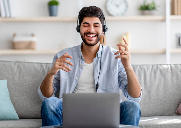 istock Distant communication concept. Happy millennial arab guy in headset talking and gesturing to laptop camera 1349984352
