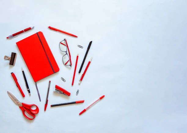 Flat lay of red notebook and stationery on blue background Flat lay of red notebook and stationery on blue background with copy space. Top view of red journal for monthly planning and creativity. School agenda and office supplies, pencils, glasses, scissors. stapled paper stock pictures, royalty-free photos & images