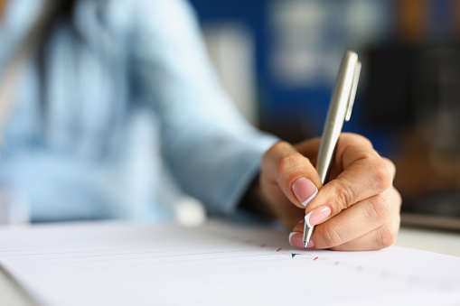 Close-up of female hand holding pen and putting green check on white paper. Application form for personal information. Red crosses and black lines on sheet. Hiring concept. Blurred background