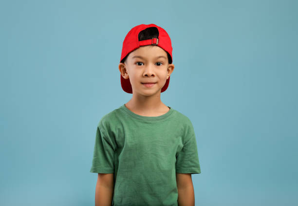 портрет милого азиатского мальчика в красной шляпе и зеленой футболке - child little boys isolated standing стоковые фото и изображения