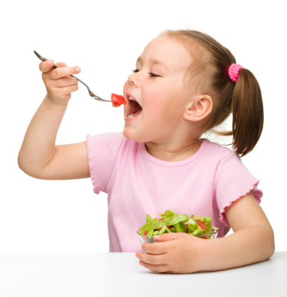Cute little girl eats vegetable salad using fork, isolated over white
