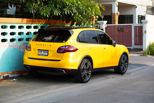 Rear view of parked yellow Porsche Hybrid car in street of Bangkok