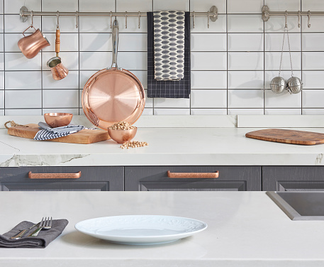 Kitchen brass utensils, chef accessories. Hanging copper kitchen with white tiles wall flower vase window and olive oil