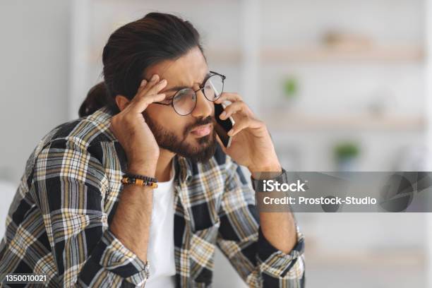 Upset Middleeastern Guy Having Phone Conversation Home Interior Stock Photo - Download Image Now