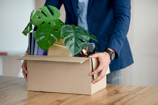 Unrecognizable young man with carton box of belongings quitting his job, changing office, receiving promotion, having first day of new work, closeup. Employment and human resources concept