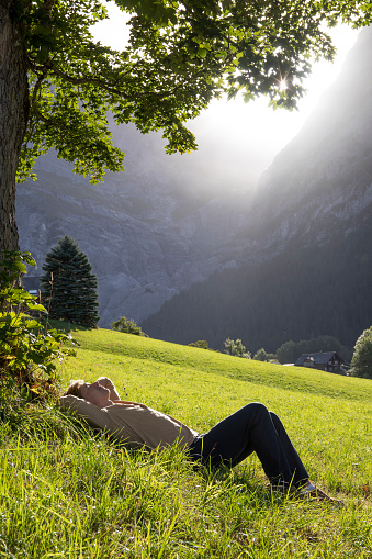 Man lying down relaxing with eyes closed and hands behind his head, feeling comfortable on the grass field