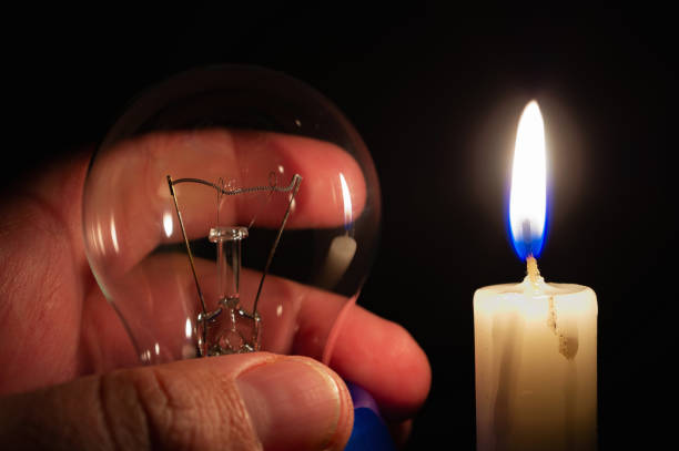 istock Not glowing light bulb illuminated by the light of a burning candle in complete darkness. 1350020268
