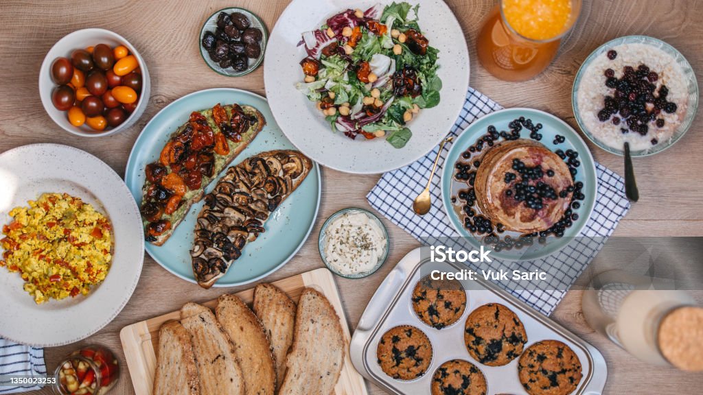 Served dining table Vegan breakfast ideas. Vegan scrambled eggs, plant milk, pancakes, salad, carrot juice and sandwiches, blueberry muffins, oatmeal and plaid dish cloth Veganism Stock Photo