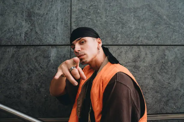 Portrait of a young adult man wearing cool urban clothes in the city. He's standing on a staircase against a grey wall.