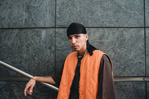 Portrait of a young adult man wearing cool urban clothes in the city Portrait of a young adult man wearing cool urban clothes in the city. He's standing on a staircase against a grey wall. italian music stock pictures, royalty-free photos & images