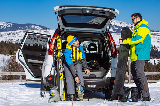 Young woman preparing for a winter hike, taking equipment from the car trunk.