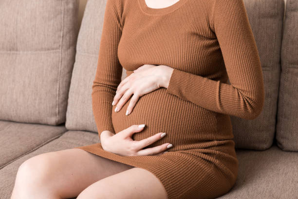 istock Pregnant Lady Having Massaging Lower belly Sitting On Sofa Indoor. Pregnancy Problems Concept. Maternity healthcare 1350032283