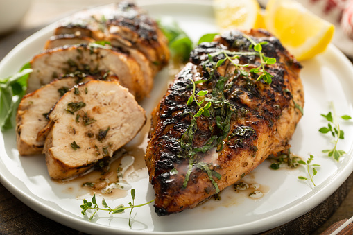 Balsamic grilled chicken breast with fresh herbs whole and sliced on a white plate
