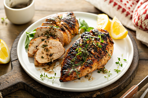 Balsamic grilled chicken breast with fresh herbs whole and sliced on a white plate