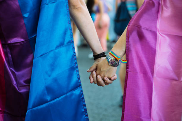 nahaufnahme von zwei mädchen, die sich an den händen halten und am gay pride day mit fahnen und armbändern demonstrieren lgbt - stroking couple desire love stock-fotos und bilder