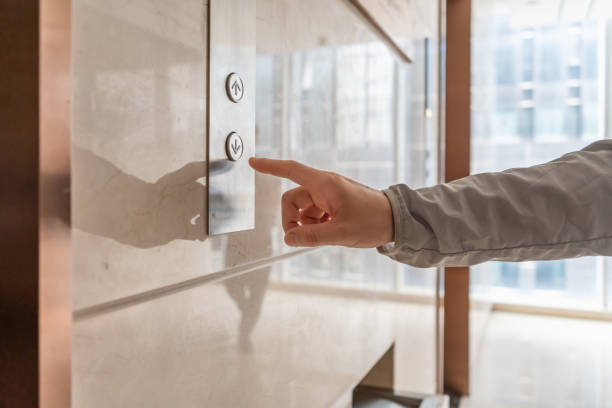 A hand at the elevator door is about to press the down button
