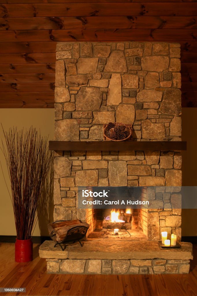 A romantic setting by a stone fireplace with candles and logs burning in the mountainside cabin. A glowing fire sets a romantic scene in a mountainside cabin in North Carolina. Fireplace Stock Photo