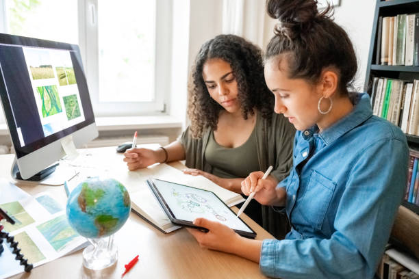две молодые женщины работают вместе над концепциями защиты климата - computer student mixed race person multi ethnic group стоковые фото и изображения