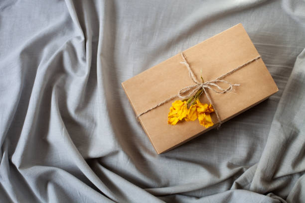 istock Simple gift packaging, craft box, ribbon twine, dry yellow flower, on grey linen fabric background. 1350038310