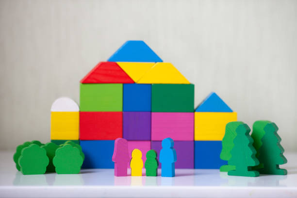 Wooden town from multicolored blocks. Wooden figures of people, family with children and multi-storey building on a background. Close up. Toys made of natural materials. Zero waste. Selective focus.