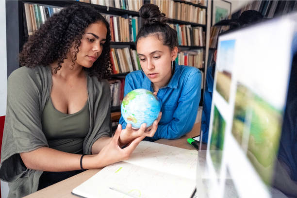 zwei junge frauen, die zusammen auf dem globus nach studien suchen - kartograph stock-fotos und bilder