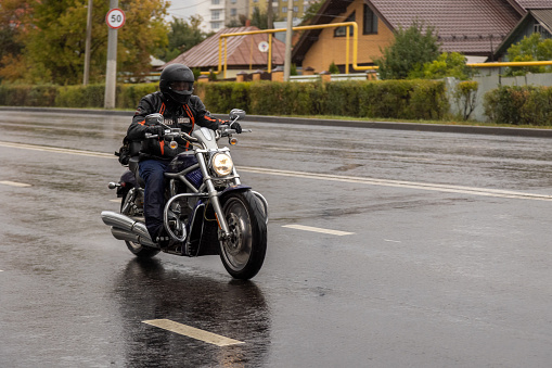 man on black chopper bike moving on wet autumn suburb road Tula, Russia, 09 19 2021