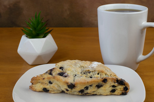 blueberry scone on a plate served with cup of coffee