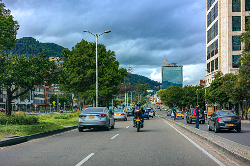 Bogotá, Colombia - October 08, 2021: The drivers point of view on Carrera Septima driving through the Usaquen area in the Andean capital city of Bogota, in South America. To the right are modern office buildings with glass windows and a hotel. Due to the amount of rainfall the capital city receives through out the year, there are healthy trees everywhere. In the far background are the Eastern Hills of The City. The altitude at street level is 8,660 feet above mean sea level. Horizontal format. Copy space.
