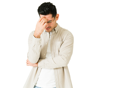 I have a bad headache. Upset man suffering from migraine while looking down and sad against a white background